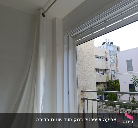 חלון עם וילון לבן ומעקה ברזל